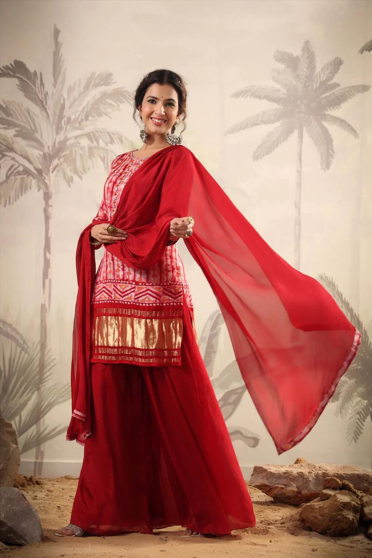 Featuring a crimson red kurti in gajji silk base with zari, gota patti, thread, sequins and stones hand embroidery. Printed Kurti with poly crepe lining. It is paired with matching georgette tiered sharara pants with poly crepe lining and a silk chiffon dupatta with fringes for a touch of elegance. Gajji silk kurta, Georgette sharara, Silk chiffon dupatta Lining: Cotton Voile Occasion: Festive Ethnic Motifs Print Pattern Ornamentation: Beads And Stones Kurta Length: 36"-37" Sharara Length: 38" S Designer Red Salwar Kameez With Dori Work, Red Unstitched Designer Wear Sharara, Traditional Georgette Palazzo Set With Cutdana, Designer Red Unstitched Sharara, Traditional Cutdana Georgette Palazzo Set, Designer Unstitched Red Sharara, Red Salwar Kameez With Dori Work Straight Kurta, Traditional Dola Silk Palazzo Set With Dori Work, Red Salwar Kameez With Gota Work For Eid