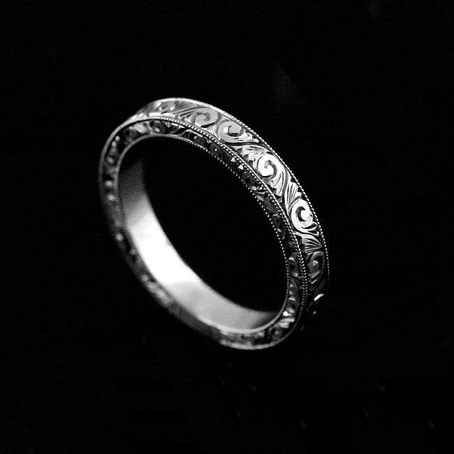 a silver ring with intricate designs on it's sides, against a black background