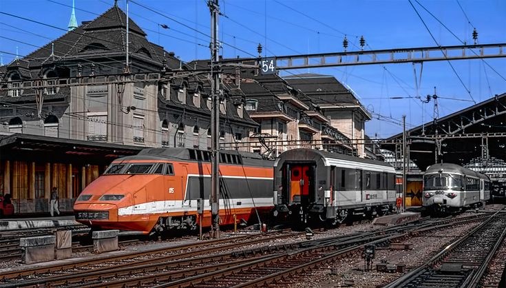 two trains are parked next to each other on the tracks in front of some buildings