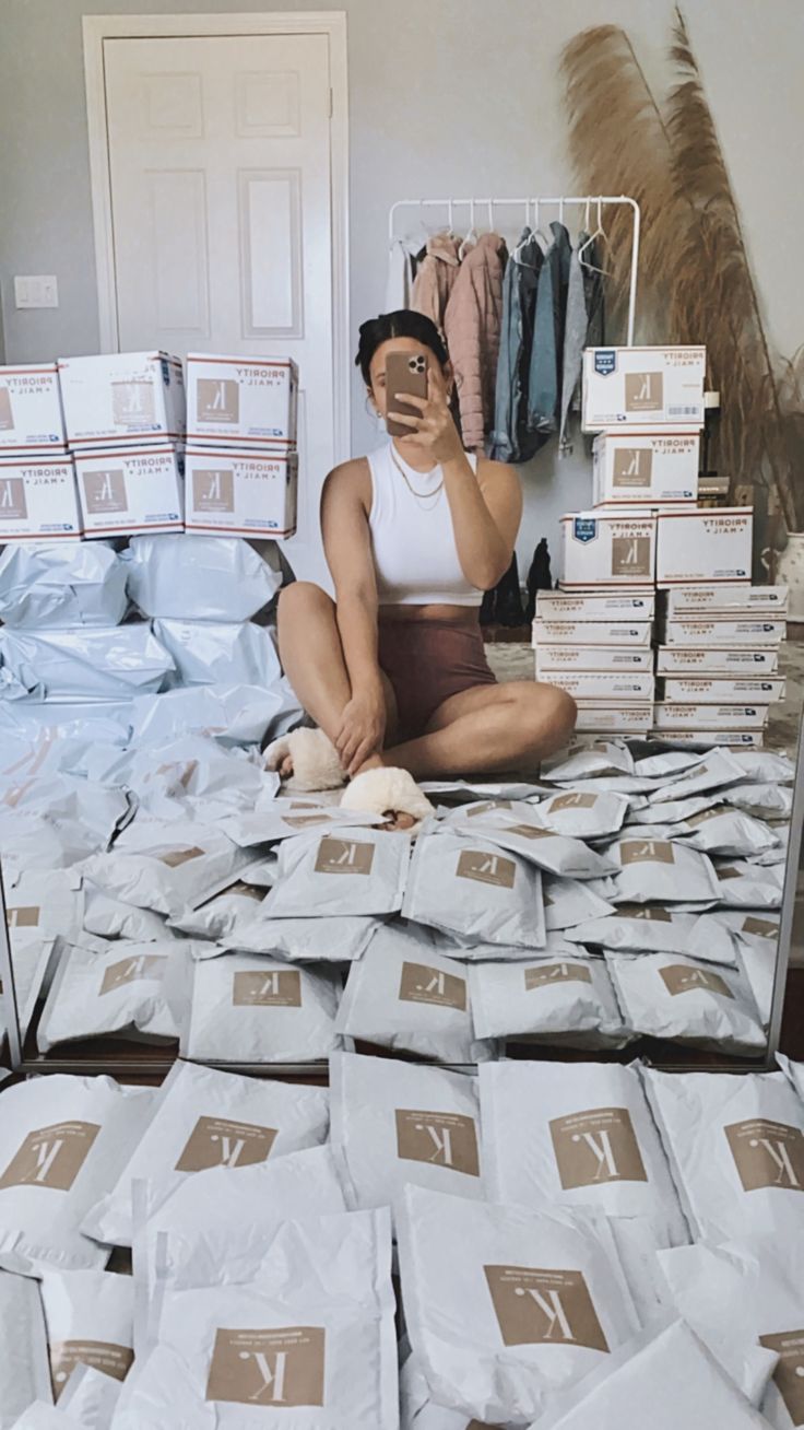 a woman sitting on the floor in front of stacks of clothes and boxes with her cell phone up to her ear