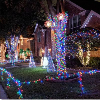 christmas lights on trees and bushes in front of a house