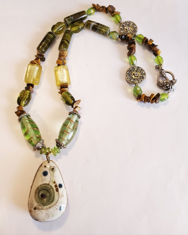 "This is an exquisite necklace made from great quality gemstones and green glass  The tubular green swirl agate gemstone measures 1\" long, 3/8\" wide. The swirl design appears brown, green and black swirl design. There are 4 in the design pattern of necklace There are 2 square shape clear light yellow beads, measures 3/8\" long, 1/2\" wide, with a touch of ivory color on the inside In the pattern there are swarvoski clear light green beads to accent the, Tiger Eye chips are in the pattern desig Green Teardrop Czech Glass Jewelry, Green Czech Glass Teardrop Jewelry, Artisan Green Jewelry With Unique Variations, Green Beaded Teardrop Pendant Jewelry, Nature-inspired Green Jade Necklaces, Unique Green Glass Necklaces, Unique Green Glass Necklace, Unique Green Natural Stone Necklace, Artisan Green Glass Beaded Necklace