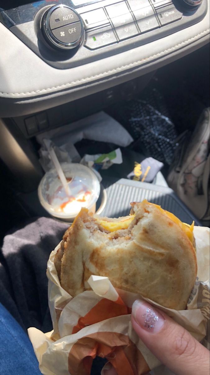 a person holding a sandwich in their hand while sitting on a car seat next to the dashboard