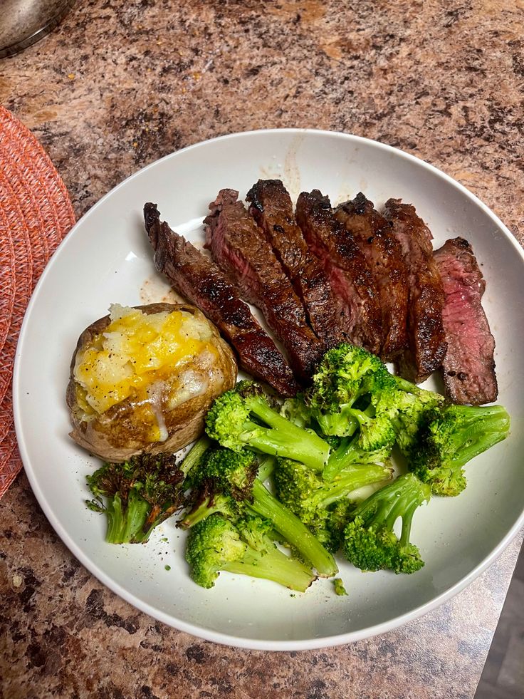 a white plate topped with steak and broccoli on top of a counter next to a knife