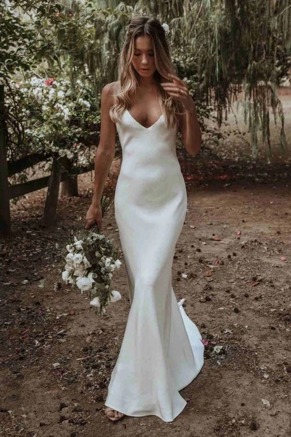 a woman in a white wedding dress is walking through the woods with her hand on her hip