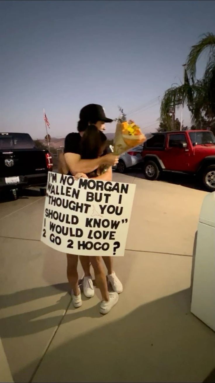 two women are holding signs in front of parked cars and one is holding a stuffed animal