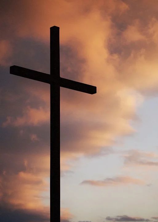 a cross on top of a wooden pole with clouds in the sky behind it at sunset