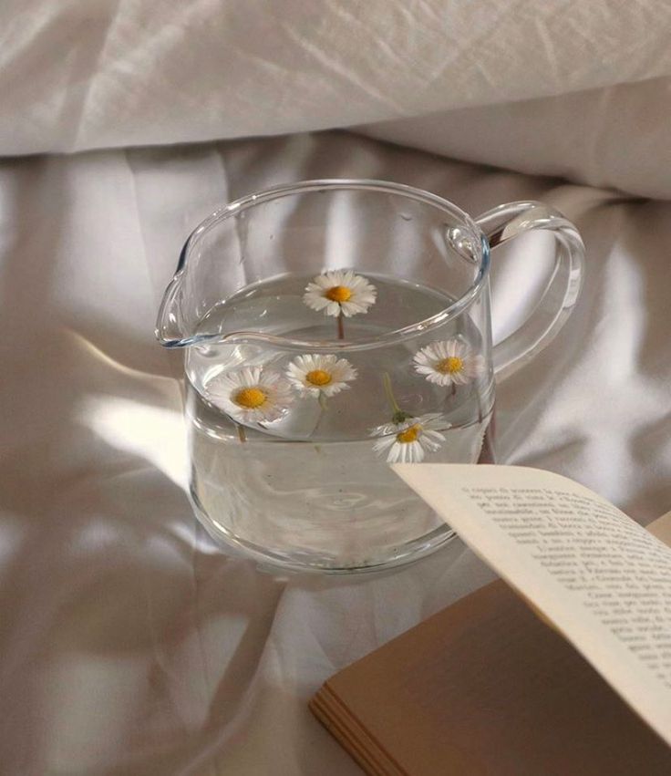 a glass pitcher filled with water sitting on top of a bed next to an open book