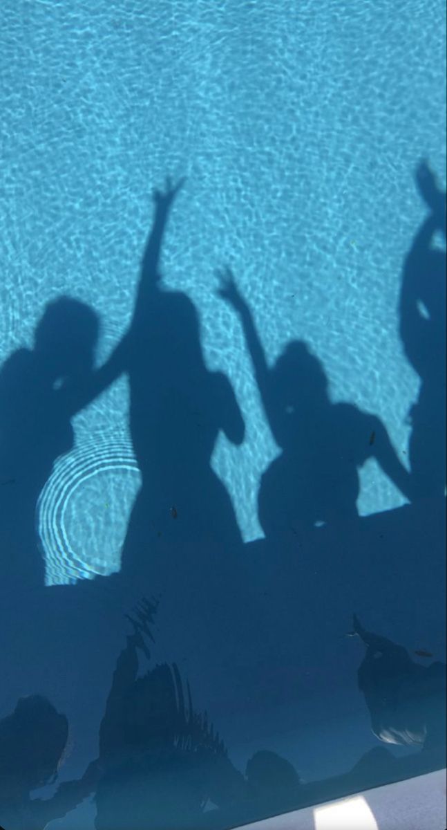 the shadow of two people standing in front of a swimming pool with their hands up