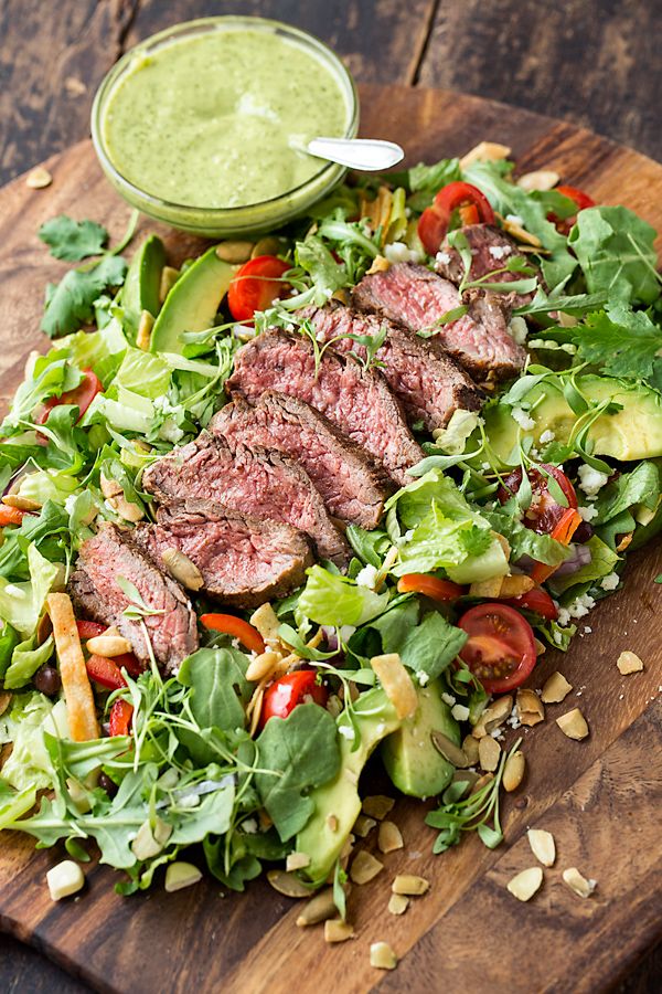 a salad with steak, lettuce and tomatoes on it is ready to be eaten