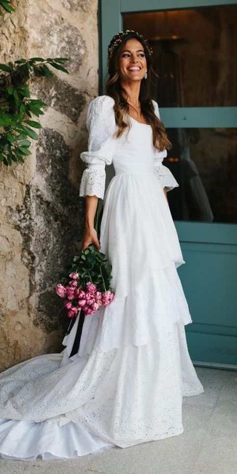 a woman standing in front of a door wearing a white dress and holding a bouquet