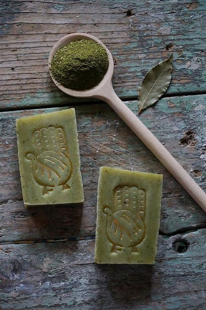 two bars of soap sitting on top of a wooden table next to a scoop of green tea