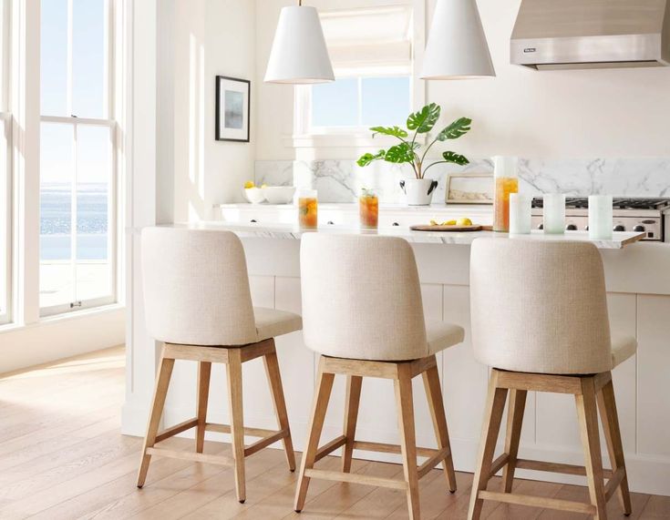 a kitchen with white walls and wooden flooring next to an island counter top, three stools on each side