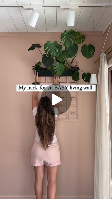 a woman standing in front of a wall with plants hanging from it's ceiling