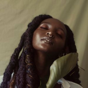 a woman with dreadlocks is holding a green leaf in her right hand and looking to the side