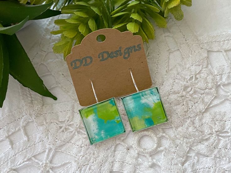 Mixed Media Art Jewelry - glass, paint, coffee filters, metal ~ These pretty turquoise and bright green art deco glass tile square earrings would be perfect for that special outfit!   The colors in these earrings are turquoise, bright green, and white.  The squares measure 5/8 inches, and the drop length is 1 3/8 inches.  Jewelry findings are silver tone. ~ Coffee filters are painted in an abstract manner with either watercolors or acrylics, or both.  Several pieces of jewelry may come from the same painted coffee filter, yet each glass tile has a different result.  Pieces are complementary, yet never match completely - making them one of a kind! ~ Painted coffee filter colors are enhanced by the glass shape and the glaze.  A tray is used as the base of the earring.  The glass with the pai Modern Green Glass Earrings, Hand Painted Green Summer Jewelry, Hand Painted Green Summer Earrings, Artistic Green Earrings For Gift, Artsy Green Earrings With Ear Wire, Artsy Green Earrings For Gift, Summer Glass Earrings For Gift, Artsy Green Earrings, Artistic Turquoise Earrings For Gift