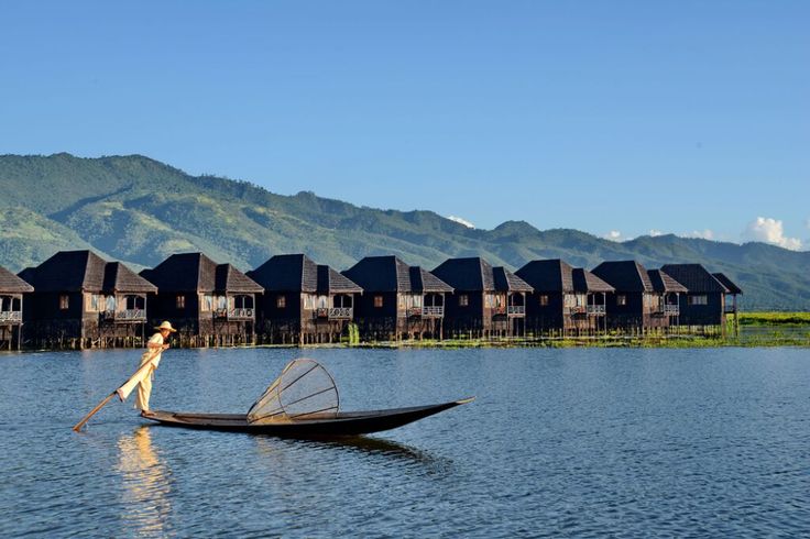 a person in a small boat on the water with houses behind them and mountains in the distance