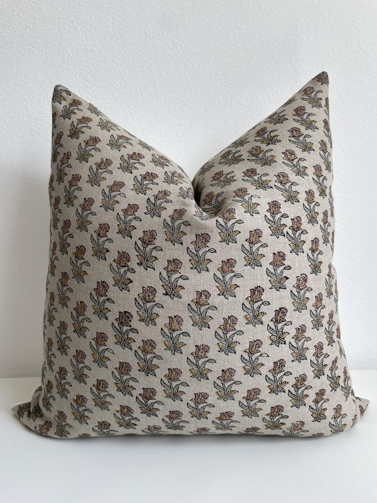 a pillow with a flower pattern on the front and back, sitting against a white wall