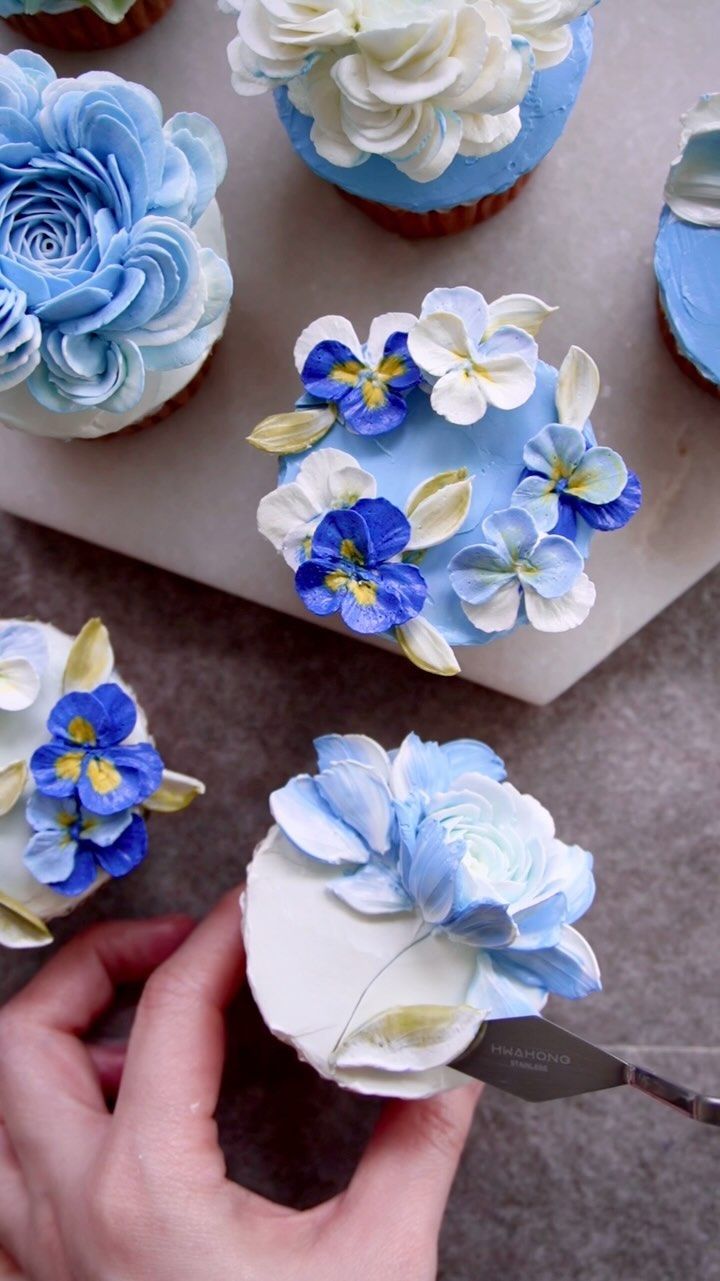 someone is decorating cupcakes with blue and white flowers