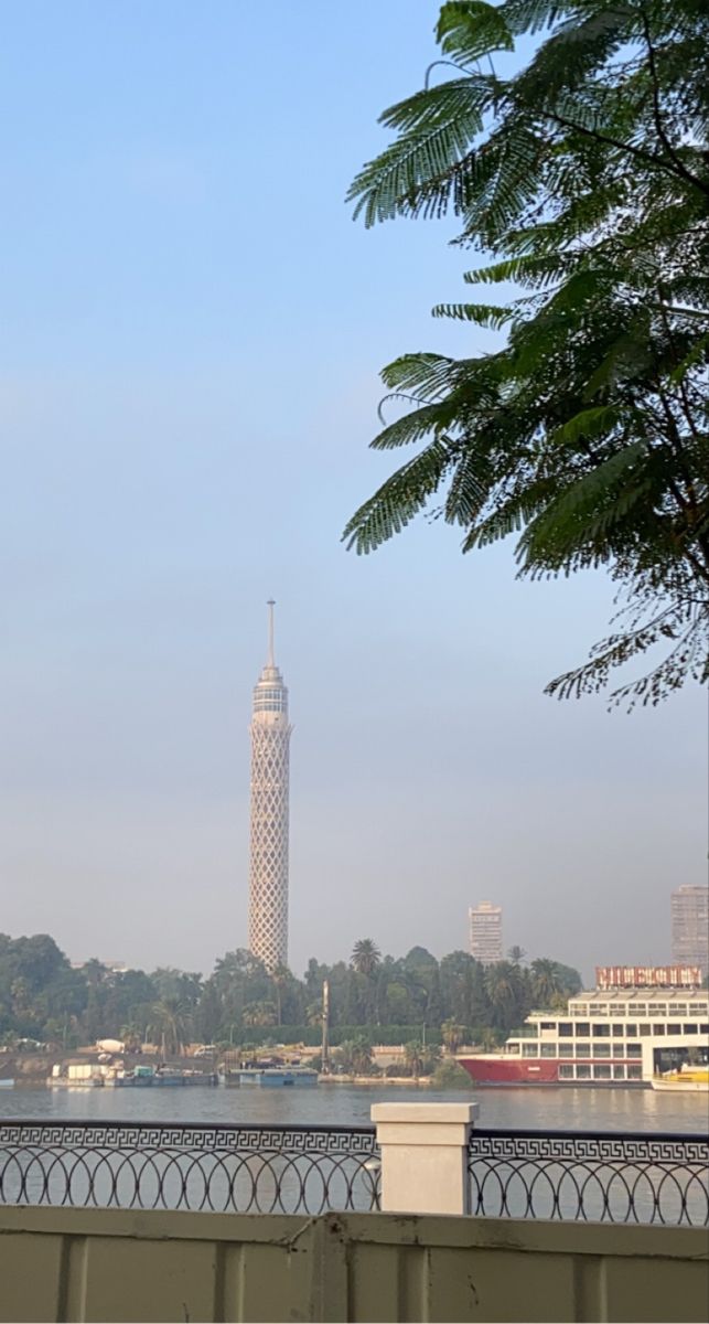 there is a clock tower in the distance behind a fenced off area with water and trees