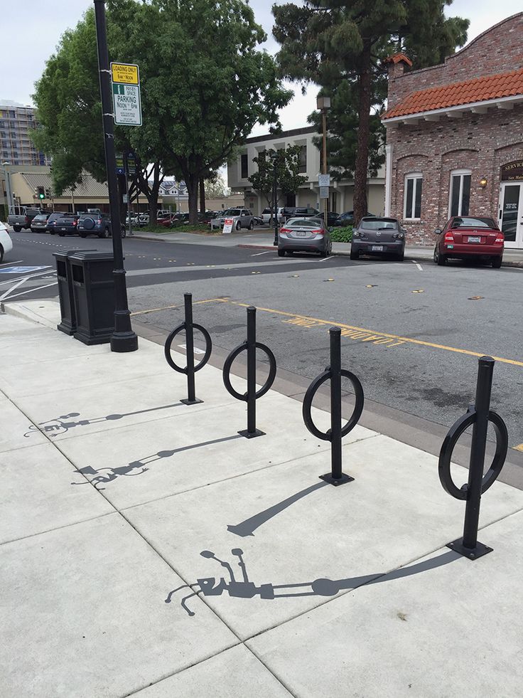 there are three black metal poles on the side of the street and one is casting a shadow