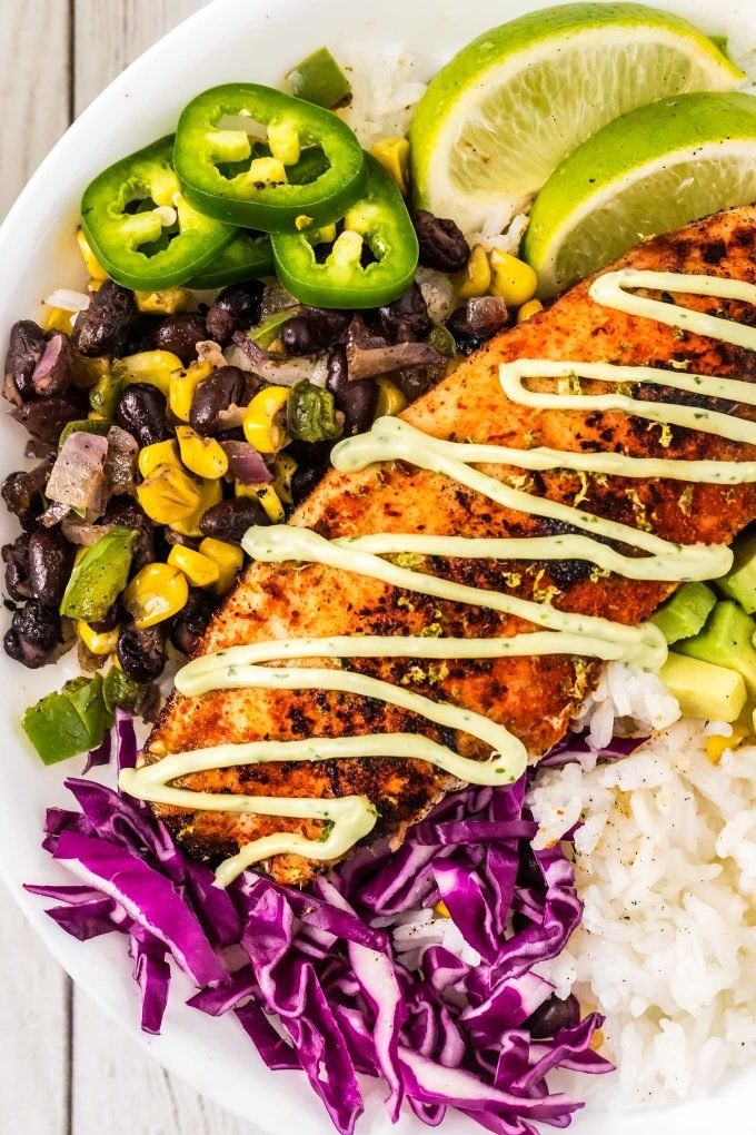 a white plate topped with fish, rice and veggies next to lime wedges