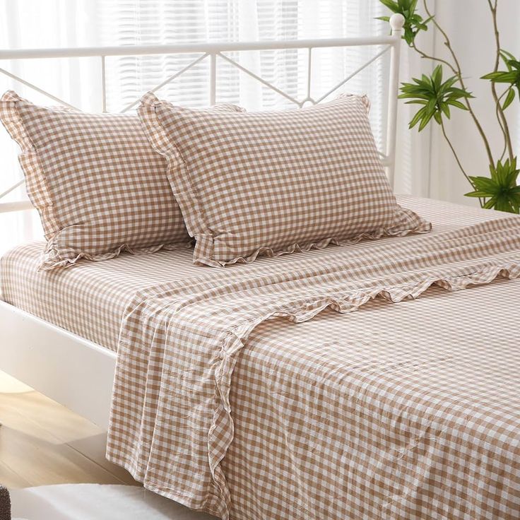 a bed with two pillows on top of it next to a potted plant and window