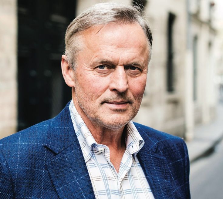 an older man in a blue suit and plaid shirt standing on the side of a street