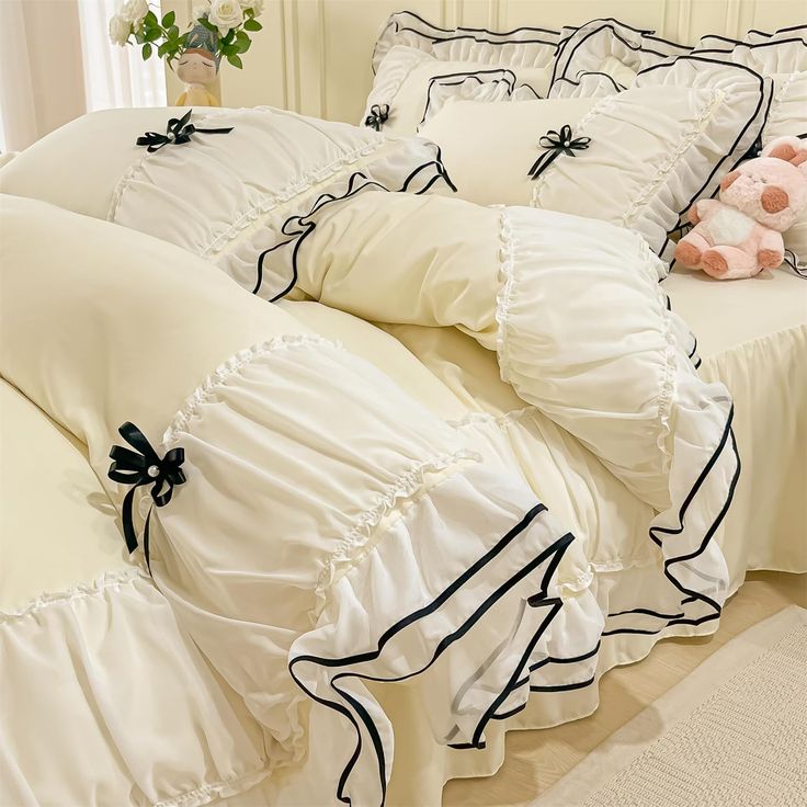 a bed with white and black ruffled sheets, pillows and a teddy bear on it