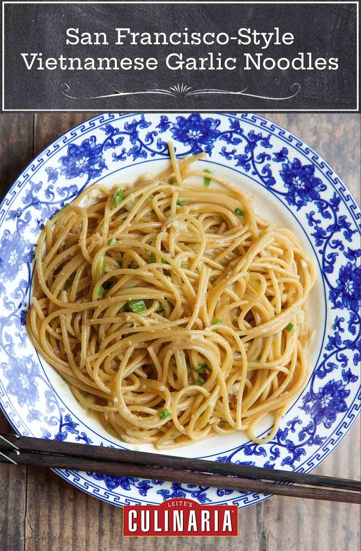 a blue and white plate filled with noodles on top of a wooden table next to chopsticks