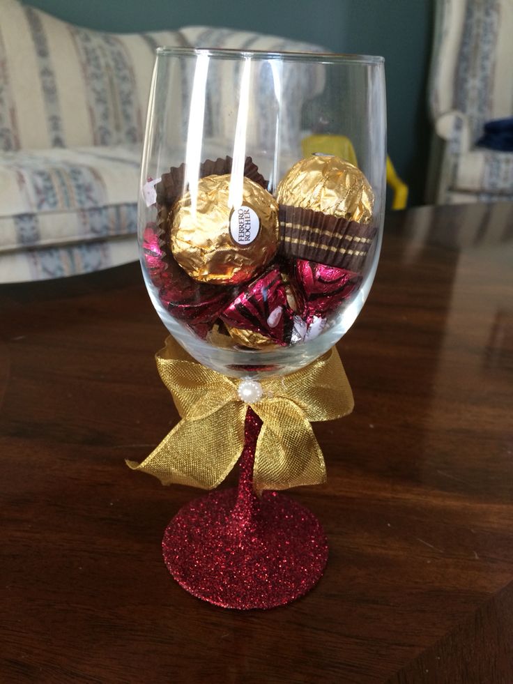 a wine glass filled with chocolates and candy on top of a wooden table next to a couch