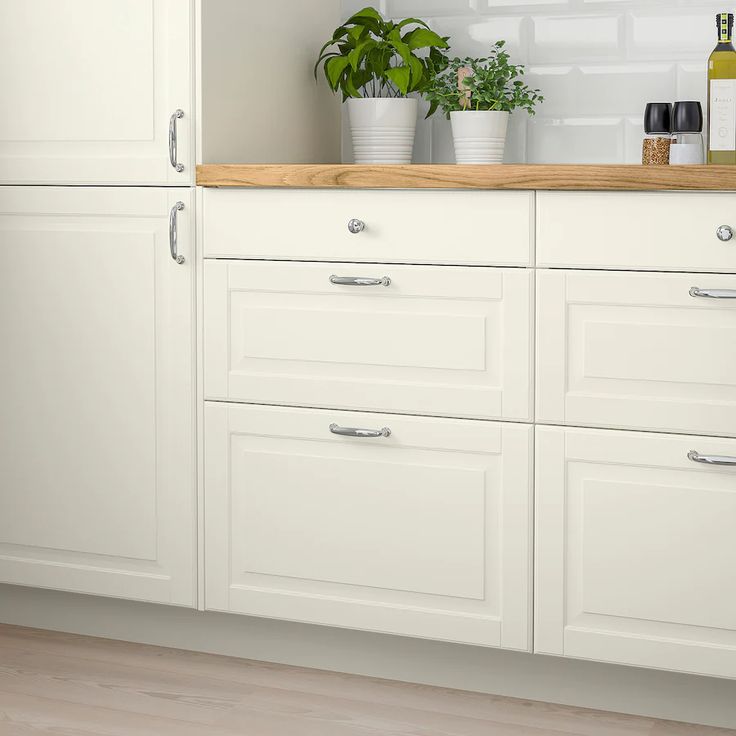 a kitchen with white cabinets and wooden counter tops, two plants in pots on top of the cabinet doors