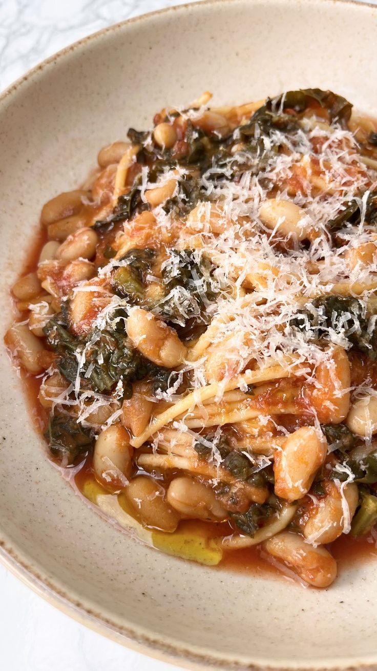 a white bowl filled with pasta and greens covered in parmesan cheese on top