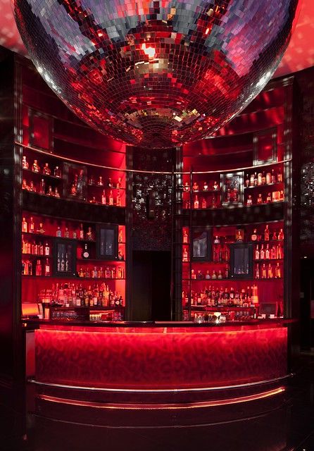 a bar with red lighting and lots of bottles on the shelves in front of it