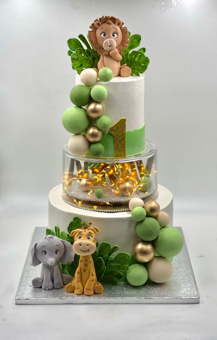 a three tiered cake decorated with green and gold decorations, including an animal figurine