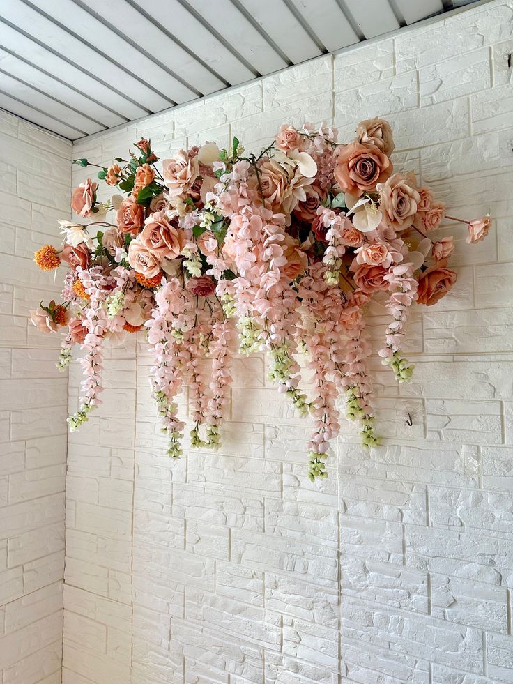 pink flowers are hanging from the ceiling in front of a white brick wall with exposed rafters