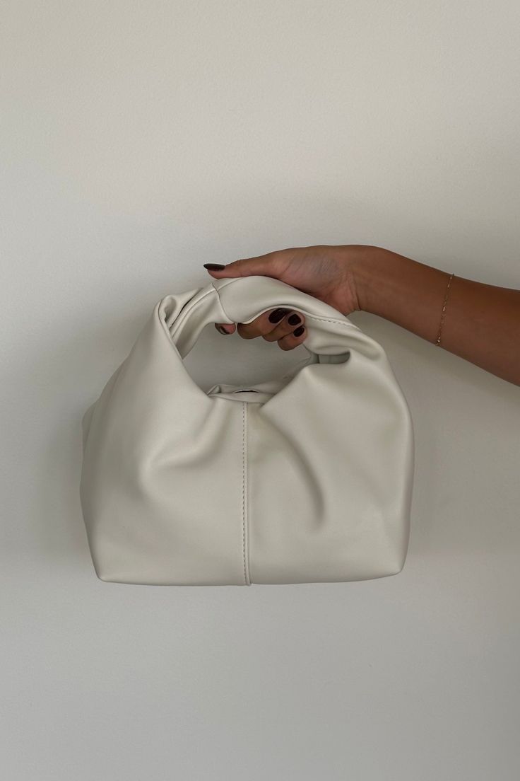 Introducing the Misty Handle Bag: a soft, semi-structured rectangular bag with a wide base, featuring two inner compartments, including a zip pouch. The top opening has a magnetic clasp closure, and the bag is highlighted by a statement wrap handle. Finished with a cotton inner lining, it combines practicality and style! Available in Bone; style with a new Fall outfit! Details: Two Inner Compartments Including with Zip Pouch Top Opening with Magnetic Clasp Closure Statement Wrap Handle Cotton In On-the-go Rectangular Soft Leather Clutch, Cream Rectangular Baguette Bag For Everyday Use, Chic Cream Shoulder Box Bag, Versatile Cream Rectangular Bucket Bag, Trendy Beige Shoulder Bag With Rolled Handles, Cream Rectangular Box Bag For Everyday, Chic Soft Leather Clutch For Shopping, Versatile Rectangular Baguette Bag For On-the-go, Everyday Cream Rectangular Box Bag