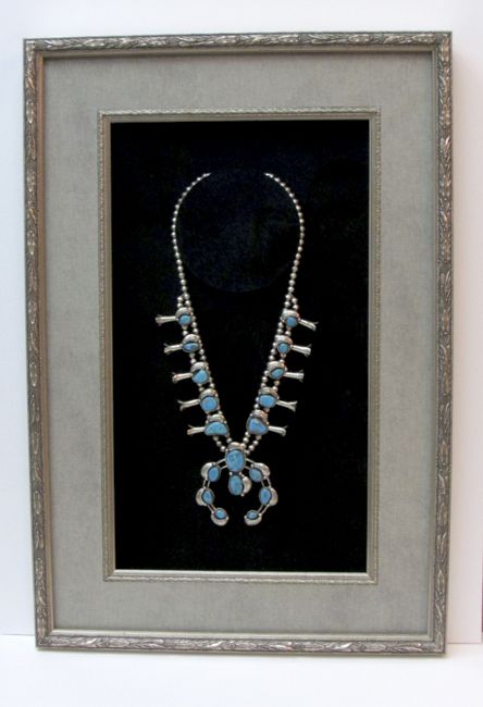 a framed photograph of a necklace with turquoise stones and silver beads on display in a gray frame