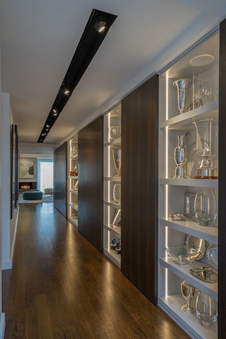 Illuminated modern shelving lines a hallway. Recessed vertical lighting and a recessed track light system in the ceiling create a contemporary display area. Modern interior design by Walker Architects. Awards Display Wall, Award Shelves, Trophy Display Shelves, Gallery Lights, Trophy Cabinets, Hallway Landing, Display Shelf Design, Trophy Shelf, Display Cabinet Design