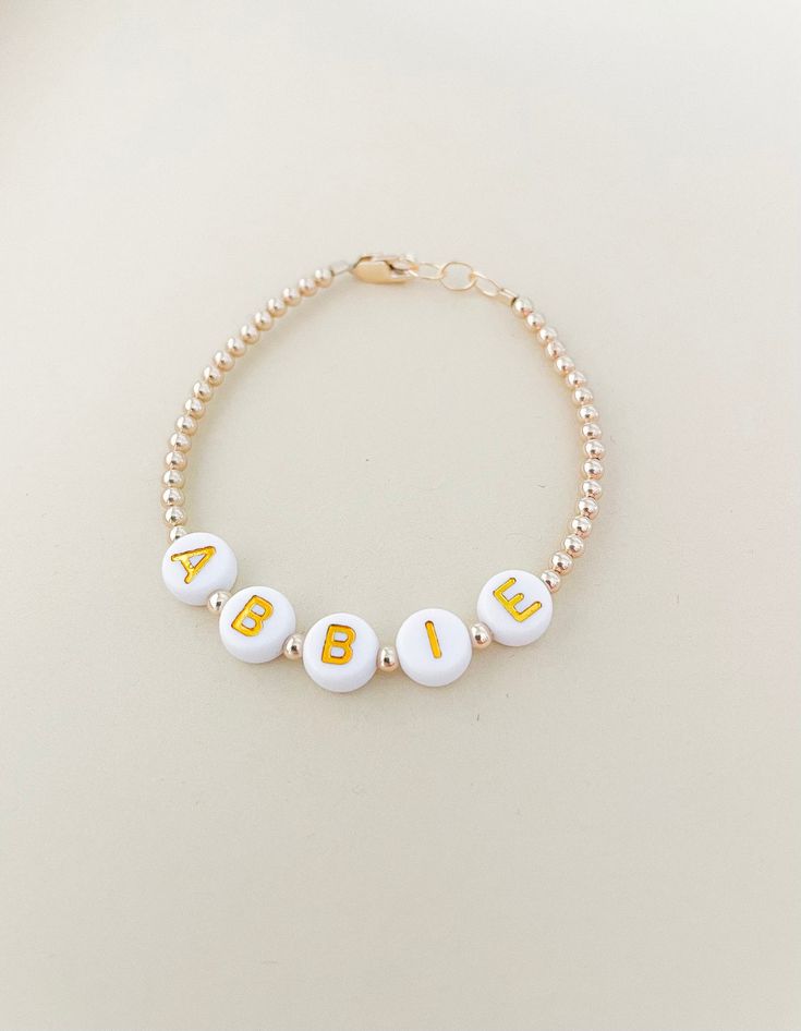 This beautiful personalized gold filled name bracelet is a perfect gift for anyone! Mamas, toddlers and children love these custom bracelets made to last. Our Bracelets are Handmade in the USA and are made with high quality gold & white letter beads with gorgeous pearl beads and 14K gold filled attachments. You will enter the custom name in the text box before adding to the cart. They are beautiful and add the perfect amount of dress up to every outfit. Each bracelet has extra links for room to Personalized Name Bracelets, Personalized Name Bracelet With Round Beads For Birthday, Personalized Round Beads Name Bracelet For Birthday, Gold Beaded Bracelet With Name For Birthday, Adjustable Yellow Gold Name Jewelry, Personalized Hypoallergenic Yellow Gold Bracelets, Gold Beaded Bracelets With Name For Birthday, Cute Custom Name Bracelet Jewelry, Gold Round Name Bracelet