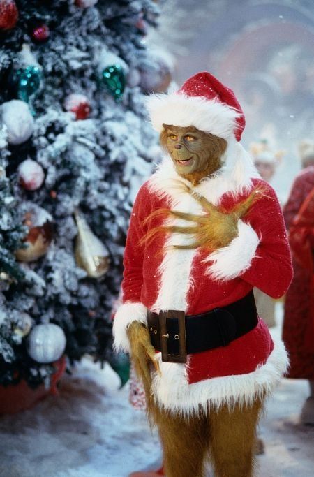 a monkey dressed as santa claus standing in front of a christmas tree with his hands on his chest