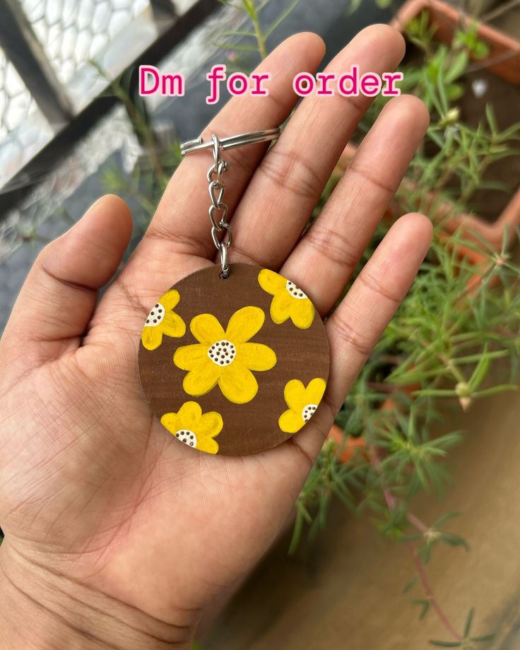 a hand holding a wooden keychain with yellow flowers painted on it and the words dm for order