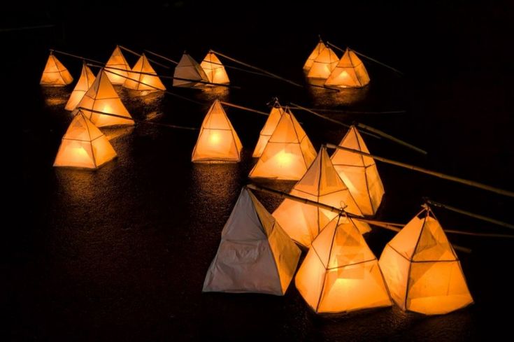 many white paper boats are floating in the dark water with lights attached to each boat