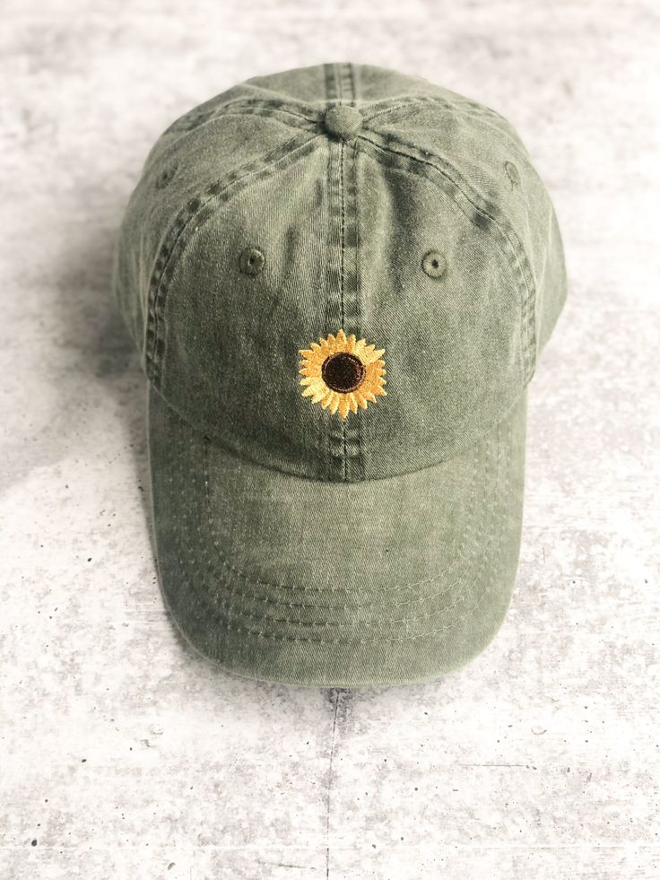 a green hat with a sunflower embroidered on the front and side, sitting on a white surface