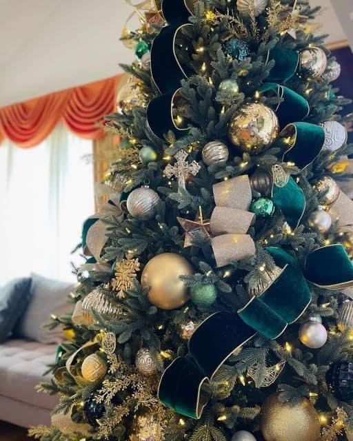 a decorated christmas tree with gold and green ornaments on it in a living room next to a couch