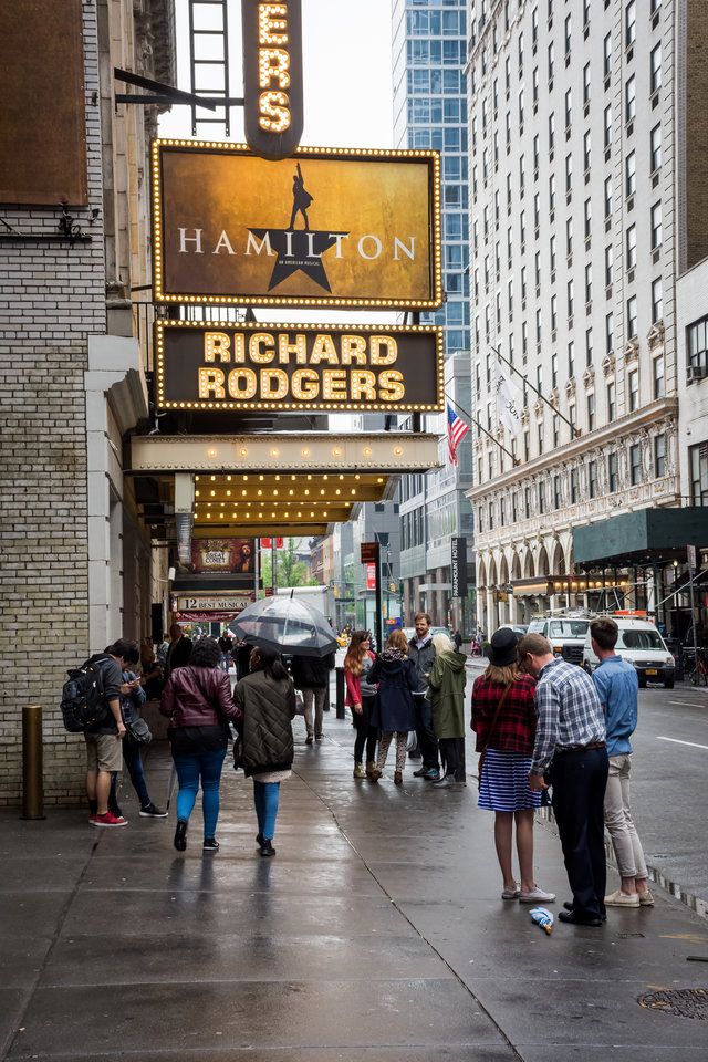 people are walking down the sidewalk in front of theater marquee