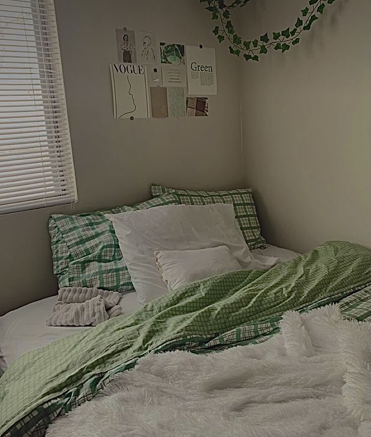 an unmade bed with green and white comforter on it in a bedroom next to a window