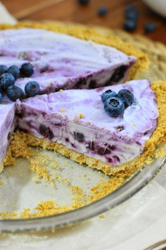 a blueberry cheesecake is cut into slices on a glass platter, with one slice missing