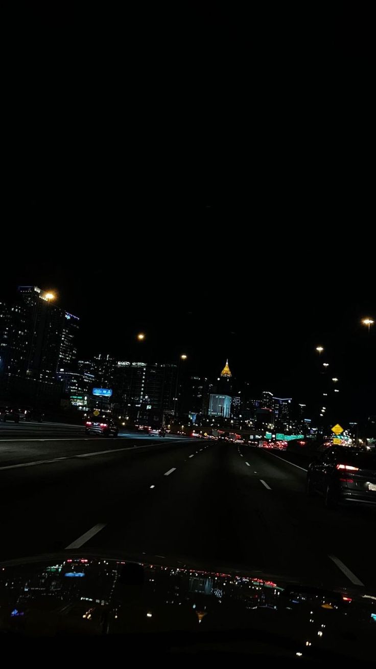 the city lights shine brightly in the dark night time sky over an empty highway with cars driving on it