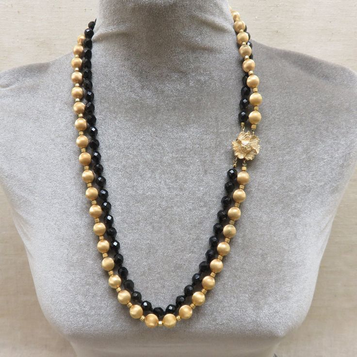 I love the elegant look of these vintage 1960 glass and metal bead necklaces. This one is a two strand necklace of 7mm faceted black glass beads mixed with 10mm brushed goldtone ball beads. The necklace measures 26 inches long. There is a lovely flower atop a box clasp and the piece is not signed by the maker. It is in excellent, near mint condition. How pretty this would look with a simple black dress or tunic top. This will arrive in a lovely gift box for easy gift giving or safe storage. If y Gold Necklaces With Round Beads For Evening, Gold Beads Jewelry For Evening, Gold Beaded Necklaces With Black Beads For Evening, Gold Beaded Necklace With Black Beads For Evening, Evening Beaded Necklaces With Polished Round Beads, Polished Beads Necklace For Evening, Evening Costume Jewelry Necklace With Faceted Beads, Evening Necklace With Polished Beads, Elegant Gold Beads With Black Details